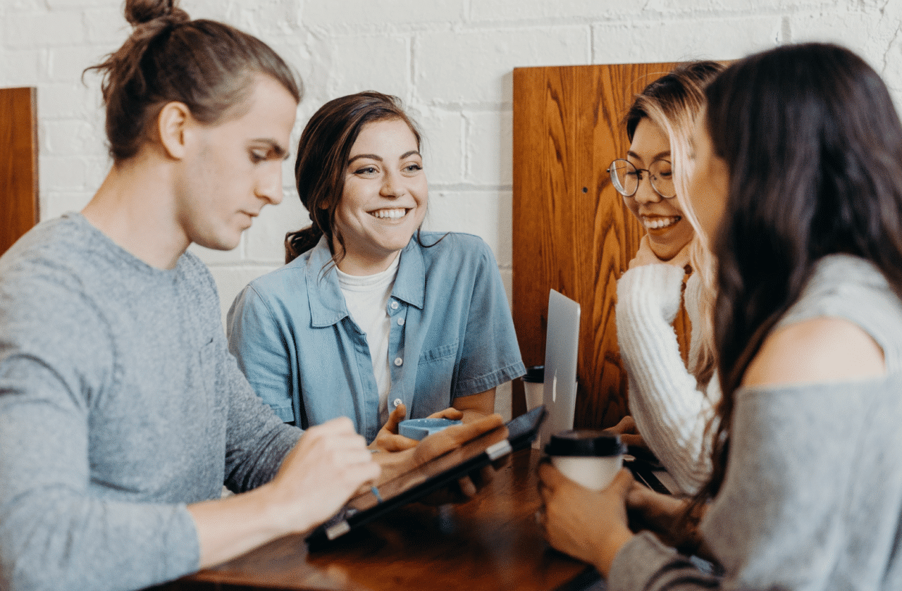 Four people sitting around a table while one of them typing on his ipad