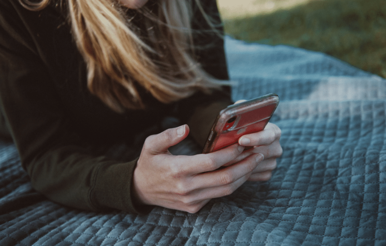Woman lying on a blanket in the park using smartphone