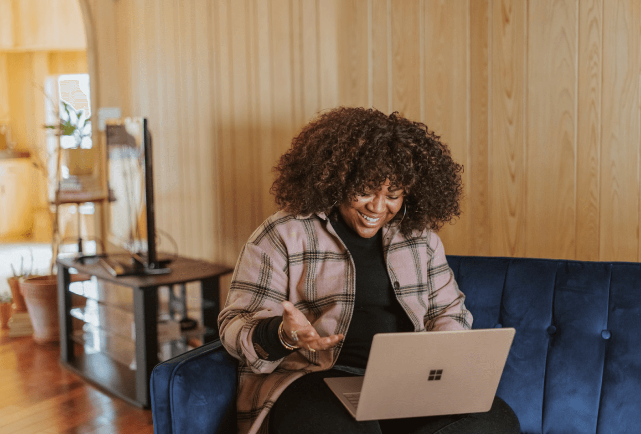 Smiling woman sitting on couch talking to someone via video call on computer