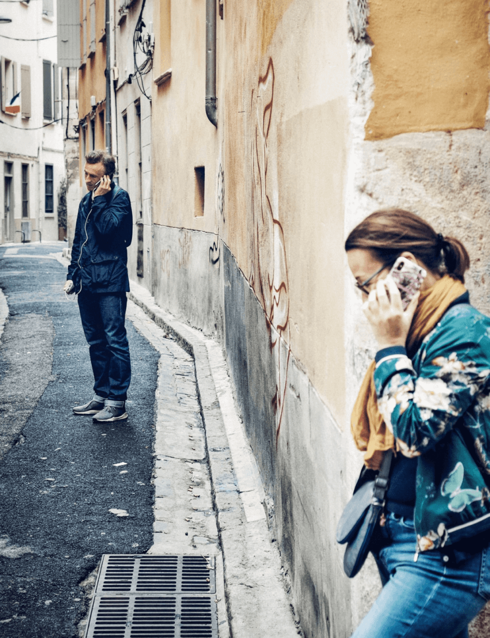 A woman and a man are on two separate phone calls in alleyway
