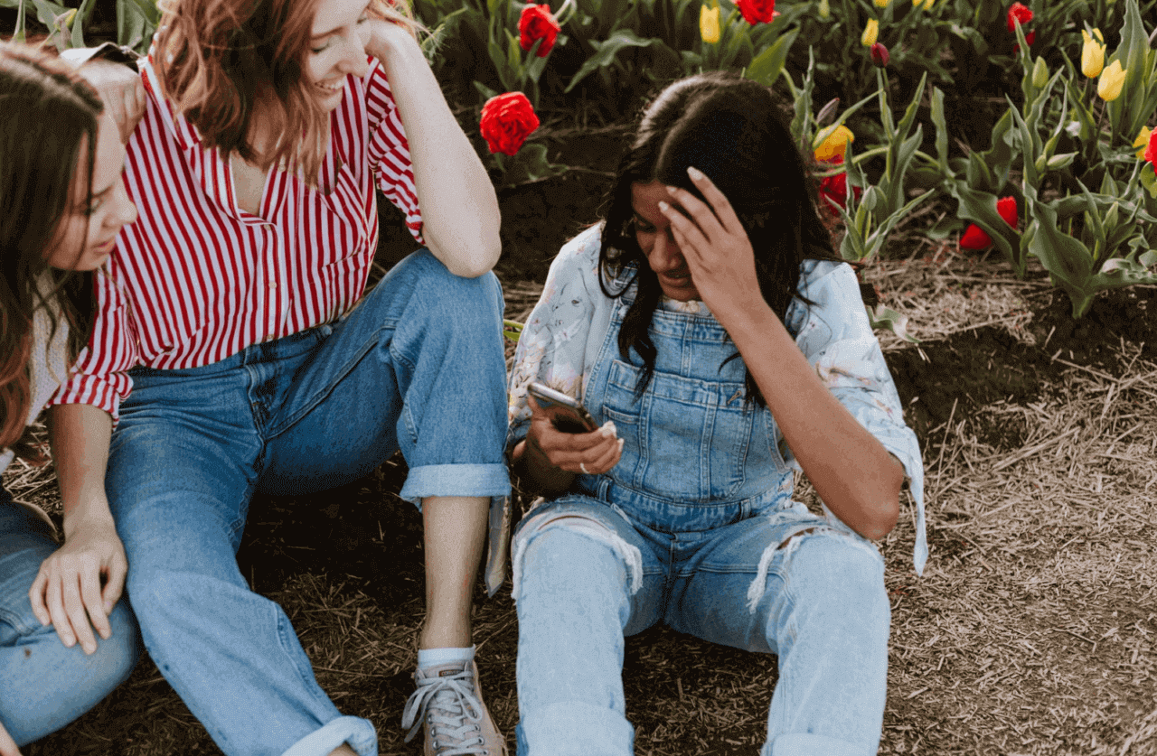 Young woman typing on her phone with her friends in a field of flowers