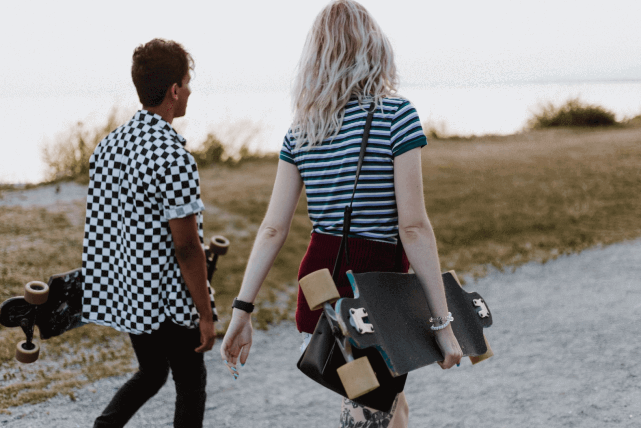 Young man and woman walking while carrying skateboards